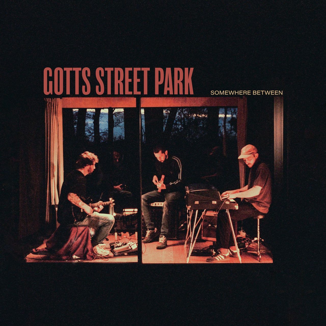 Album cover for Somewhere Between by Gotts Street Park featuring the band playing instruments in a dimly lit room.